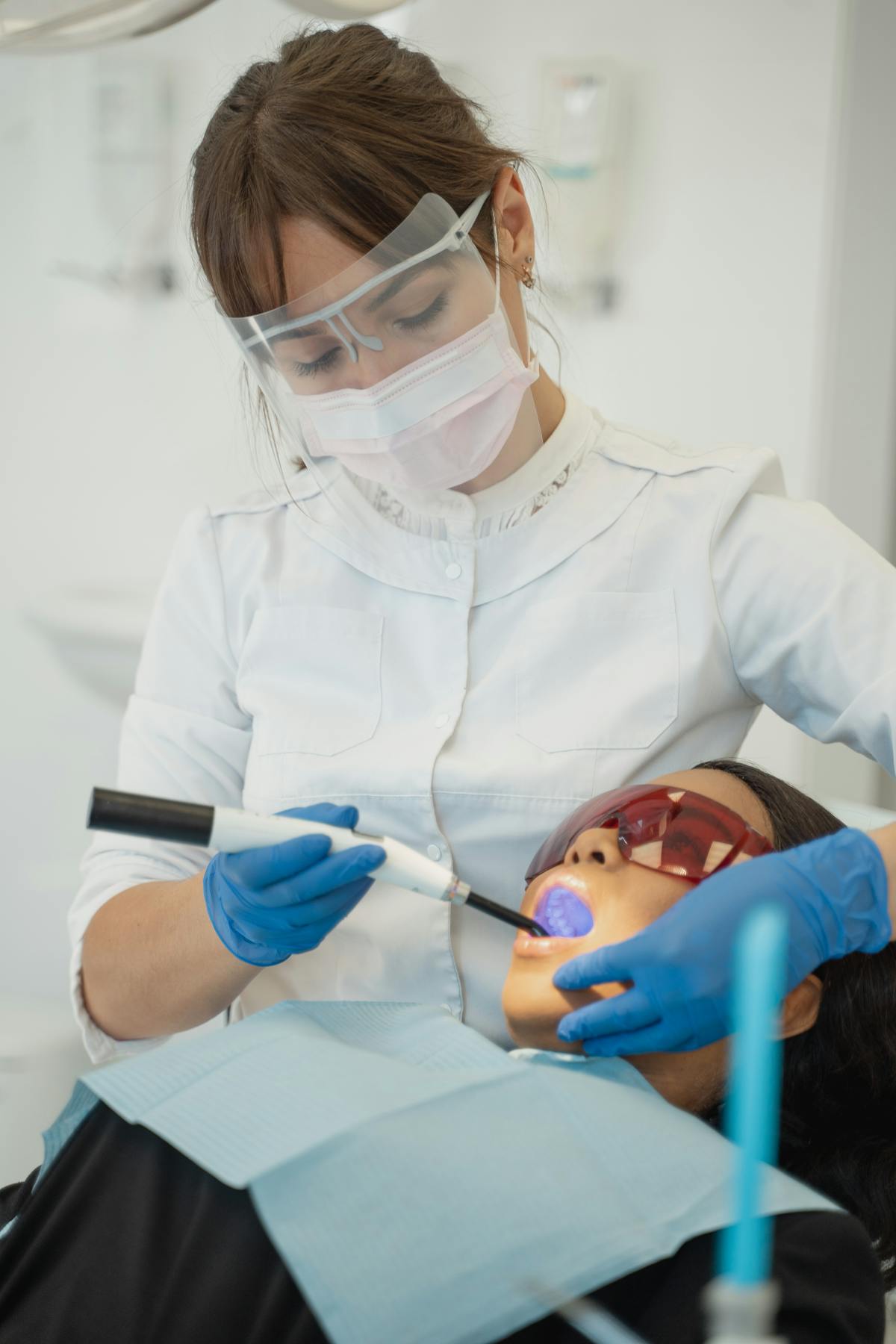 Dentist performing dental procedure with UV curing light in modern clinic